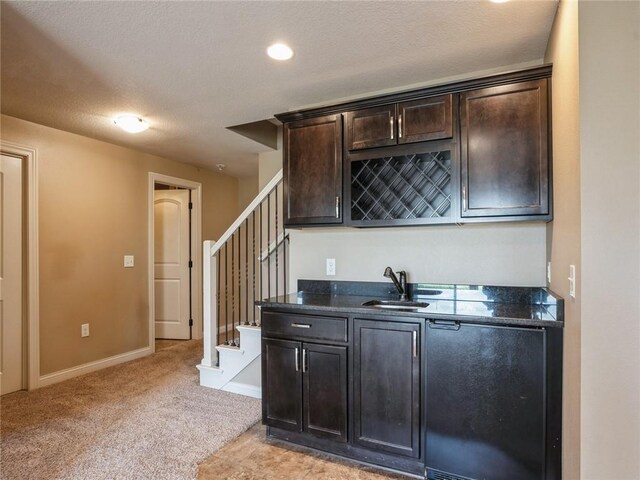 bar with dark brown cabinetry, sink, a textured ceiling, and light colored carpet