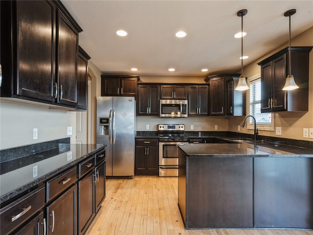 kitchen featuring stainless steel appliances, hanging light fixtures, sink, dark brown cabinetry, and light hardwood / wood-style flooring