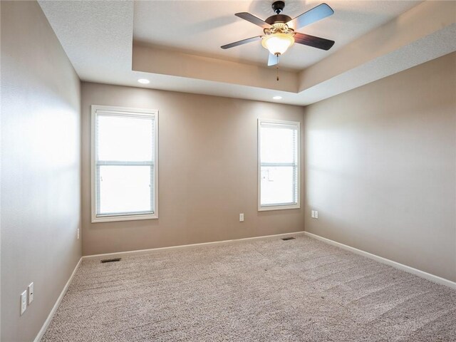 spare room with a tray ceiling, carpet floors, and ceiling fan