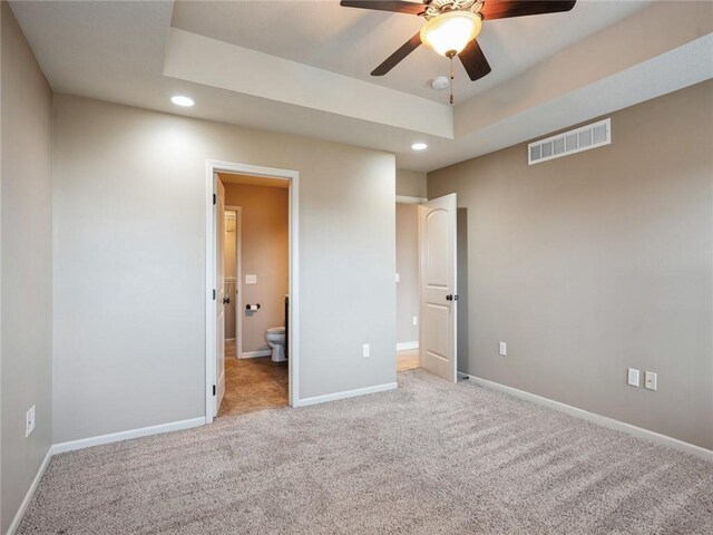 unfurnished bedroom featuring ensuite bathroom, a tray ceiling, ceiling fan, and light colored carpet