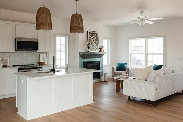 kitchen featuring a center island with sink, decorative light fixtures, white cabinetry, and appliances with stainless steel finishes