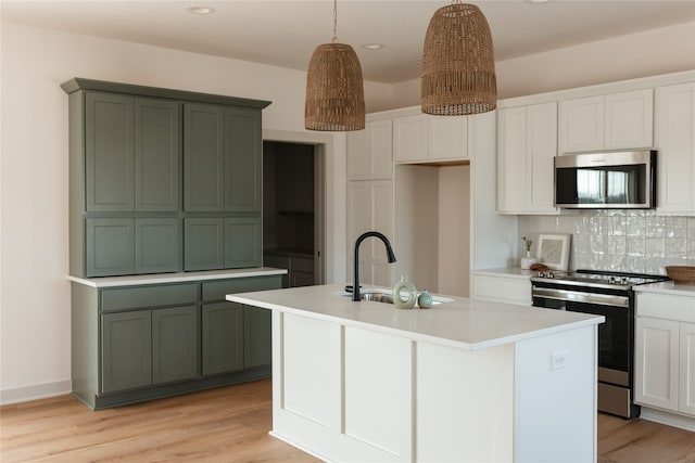 kitchen with decorative light fixtures, light wood-type flooring, stainless steel appliances, and a kitchen island with sink