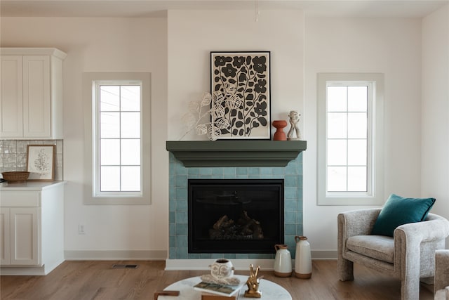 living room featuring a healthy amount of sunlight, a tiled fireplace, and light hardwood / wood-style flooring