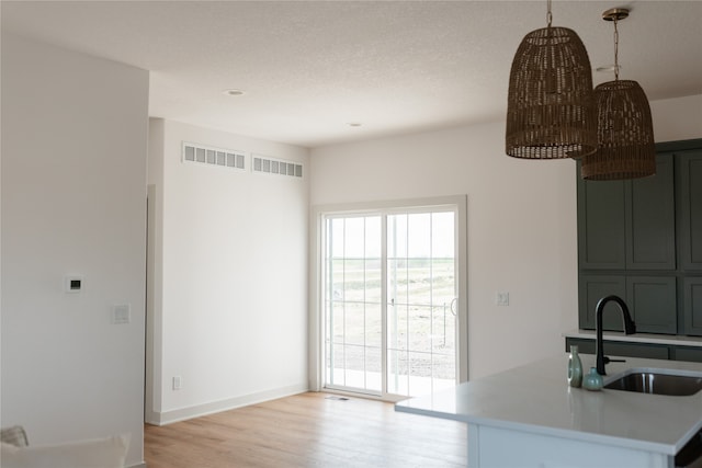 kitchen featuring sink, hanging light fixtures, light hardwood / wood-style flooring, a textured ceiling, and kitchen peninsula