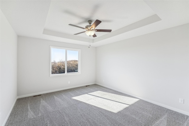 carpeted empty room featuring visible vents, a ceiling fan, a raised ceiling, and baseboards