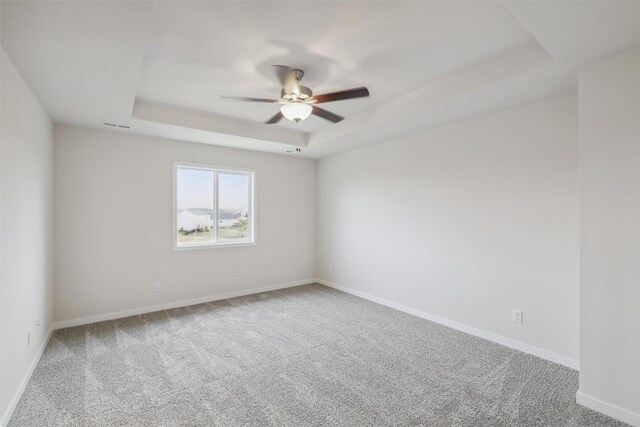 carpeted empty room with a raised ceiling and ceiling fan