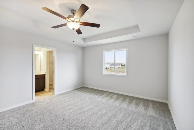 unfurnished bedroom featuring ceiling fan, light colored carpet, a tray ceiling, and ensuite bath