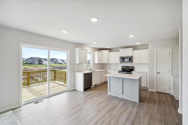 kitchen featuring light wood-type flooring, stainless steel appliances, sink, a center island, and white cabinetry