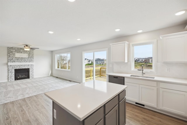 kitchen featuring a stone fireplace, black dishwasher, sink, and white cabinets