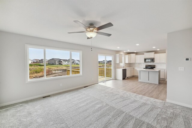 unfurnished living room with ceiling fan, sink, and light wood-type flooring