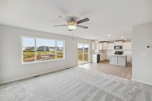 unfurnished living room with sink, light colored carpet, and ceiling fan