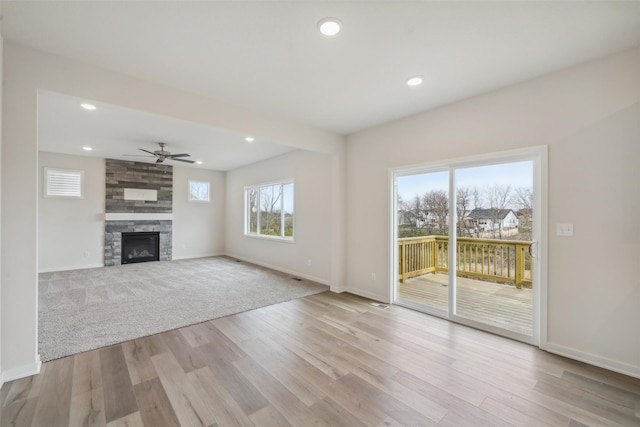 unfurnished living room featuring light hardwood / wood-style flooring, ceiling fan, and a stone fireplace