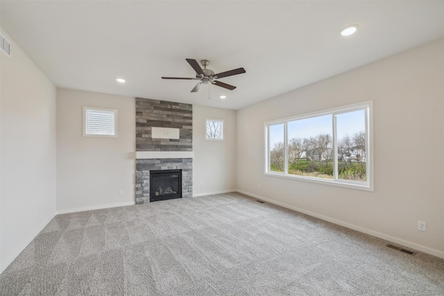 unfurnished living room with a stone fireplace, ceiling fan, and carpet