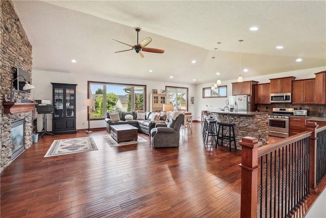 living room with ceiling fan, dark hardwood / wood-style flooring, a stone fireplace, and high vaulted ceiling