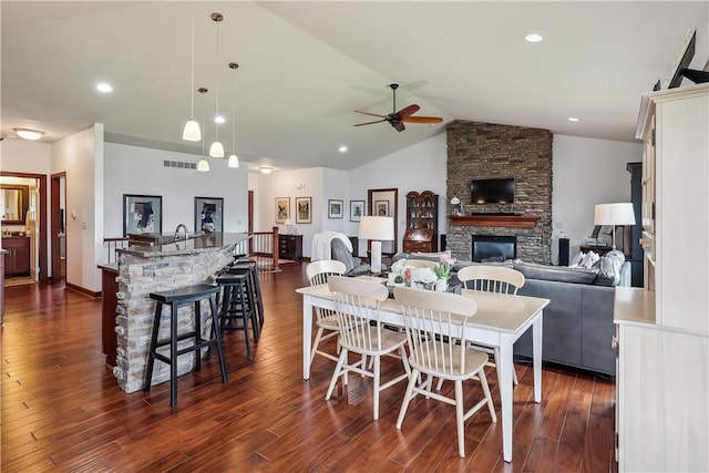 dining room featuring a stone fireplace, ceiling fan, dark hardwood / wood-style floors, and lofted ceiling