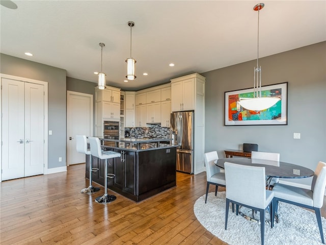 kitchen with a center island with sink, tasteful backsplash, appliances with stainless steel finishes, and light wood-type flooring