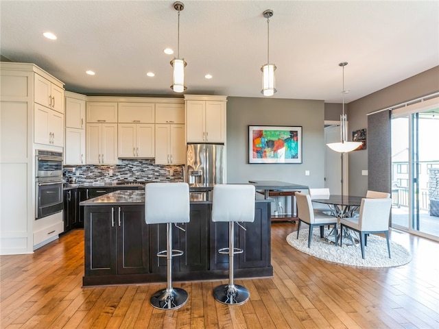 kitchen with appliances with stainless steel finishes, light hardwood / wood-style flooring, decorative light fixtures, and tasteful backsplash