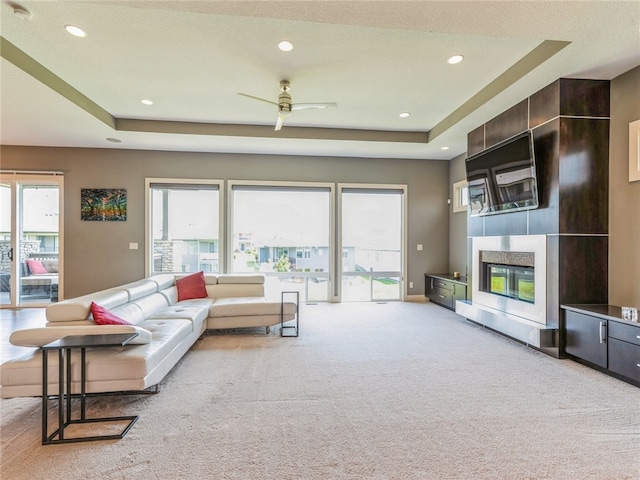 living room featuring light carpet, a tiled fireplace, and a tray ceiling