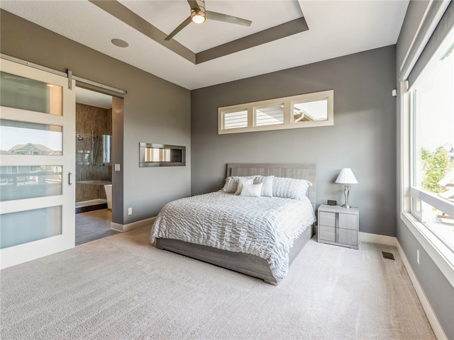 carpeted bedroom featuring a raised ceiling, ensuite bathroom, a barn door, and ceiling fan