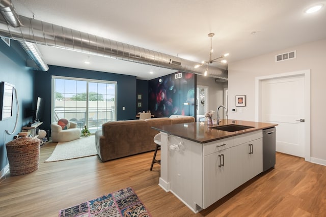 kitchen with stainless steel dishwasher, white cabinetry, light wood-type flooring, sink, and a kitchen island with sink