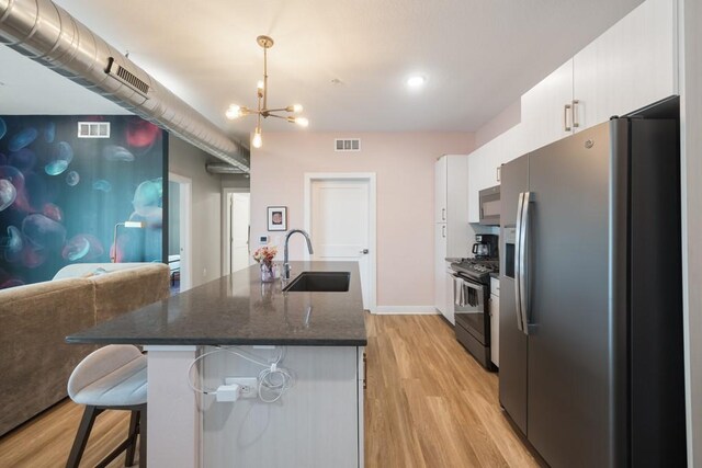 kitchen featuring appliances with stainless steel finishes, light hardwood / wood-style flooring, white cabinets, a breakfast bar, and sink