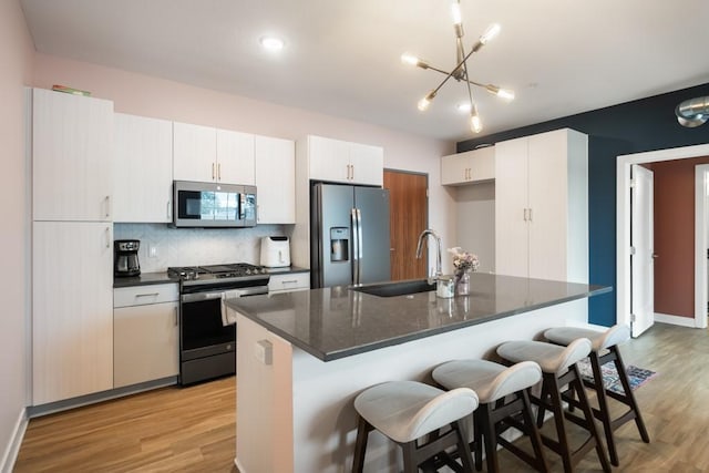 kitchen with white cabinetry, stainless steel appliances, sink, and a center island with sink