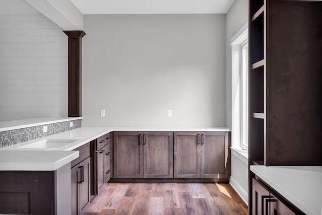 kitchen with dark brown cabinets, kitchen peninsula, light hardwood / wood-style flooring, and tasteful backsplash