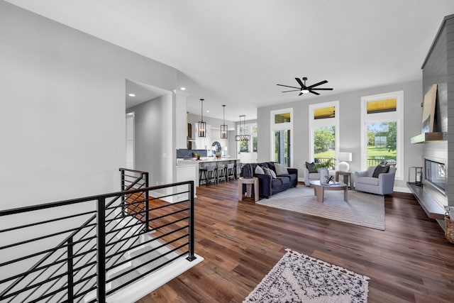 living room featuring dark wood-type flooring, ceiling fan, and a large fireplace