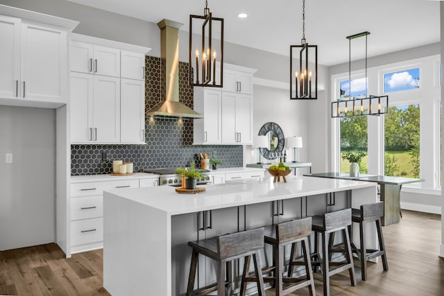 kitchen featuring hardwood / wood-style floors, backsplash, a kitchen island, white cabinetry, and wall chimney exhaust hood