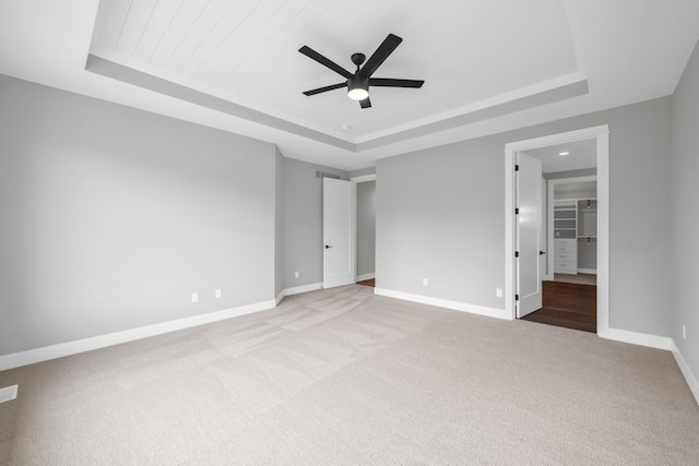 unfurnished bedroom with light carpet, ceiling fan, and a raised ceiling