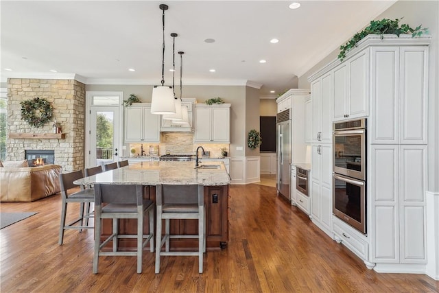 4701 150th St, Urbandale, IA 50323 - kitchen featuring stainless steel appliances, ornamental molding, white cabinets, a sink, and a stone fireplace