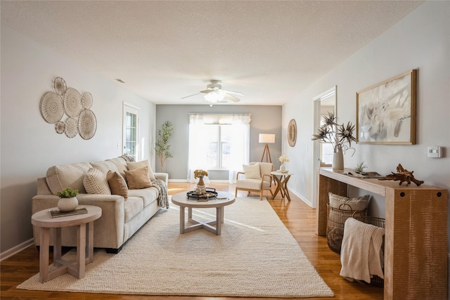 living area with visible vents, ceiling fan, baseboards, wood finished floors, and a textured ceiling