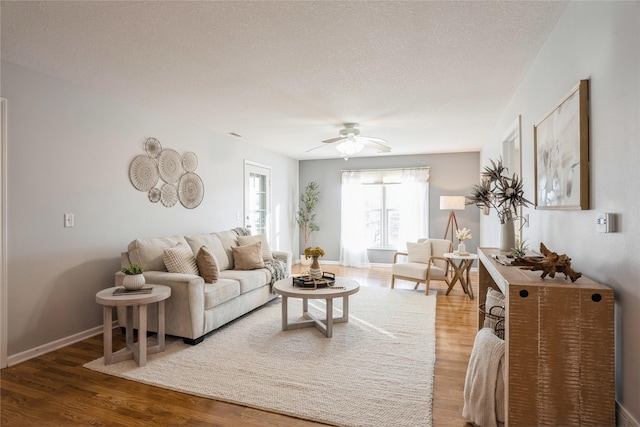 living room with ceiling fan, a textured ceiling, baseboards, and wood finished floors