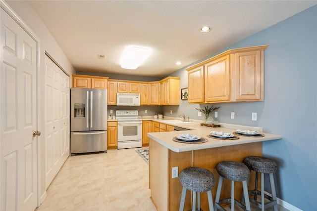 kitchen with light brown cabinets, light countertops, a peninsula, white appliances, and a sink