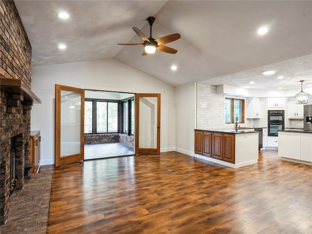 unfurnished living room with ceiling fan, brick wall, lofted ceiling, a brick fireplace, and dark wood-type flooring