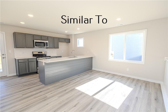 kitchen with appliances with stainless steel finishes, light countertops, a sink, and gray cabinetry