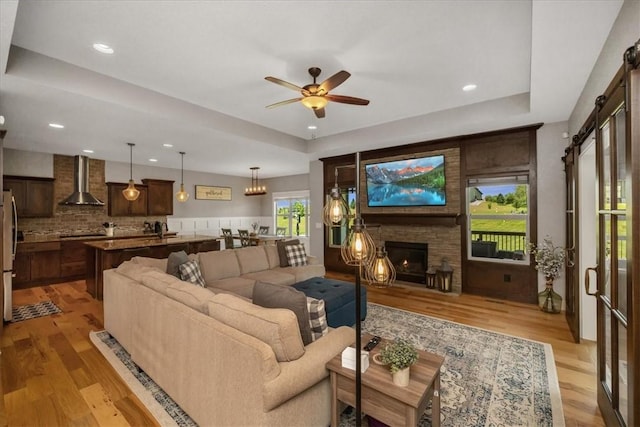 living room featuring ceiling fan, a barn door, a stone fireplace, and light hardwood / wood-style flooring