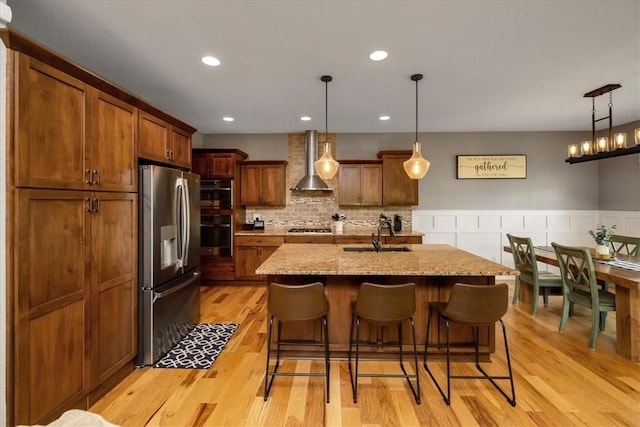 kitchen featuring wall chimney range hood, decorative backsplash, light hardwood / wood-style flooring, sink, and stainless steel appliances