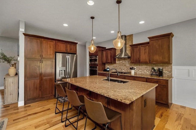 kitchen featuring decorative backsplash, light hardwood / wood-style flooring, wall chimney exhaust hood, a kitchen island with sink, and stainless steel appliances