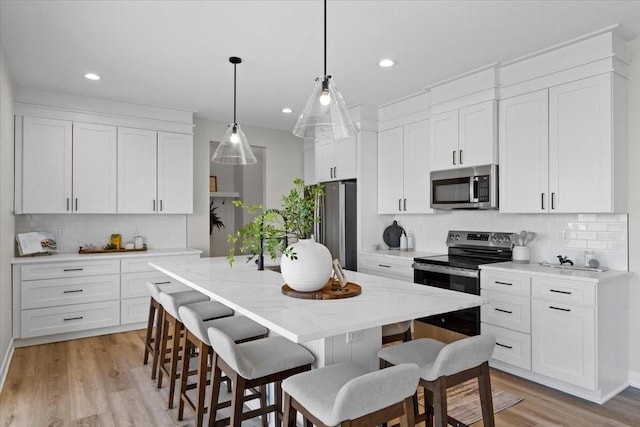 kitchen featuring pendant lighting, a kitchen breakfast bar, stainless steel appliances, an island with sink, and white cabinets