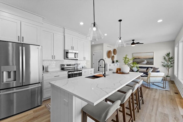 kitchen featuring white cabinetry, appliances with stainless steel finishes, light stone counters, and a center island with sink