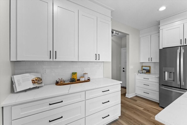 kitchen with stainless steel refrigerator with ice dispenser, white cabinetry, light stone counters, light hardwood / wood-style floors, and backsplash