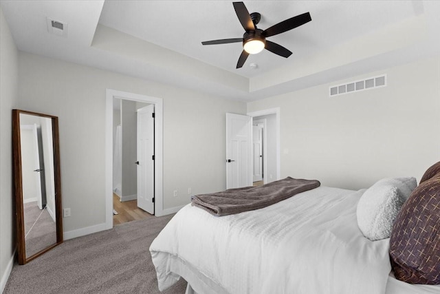 carpeted bedroom featuring a raised ceiling, connected bathroom, and ceiling fan