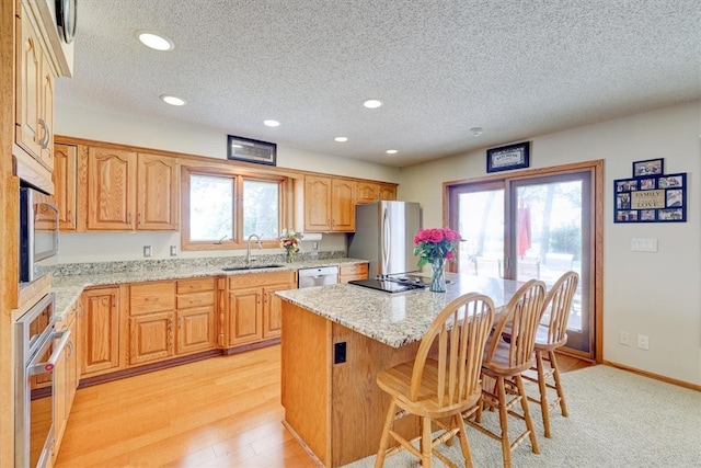 kitchen with light stone countertops, light hardwood / wood-style flooring, a center island, stainless steel appliances, and sink