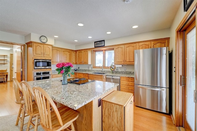 kitchen featuring a center island, appliances with stainless steel finishes, light hardwood / wood-style floors, sink, and a kitchen breakfast bar