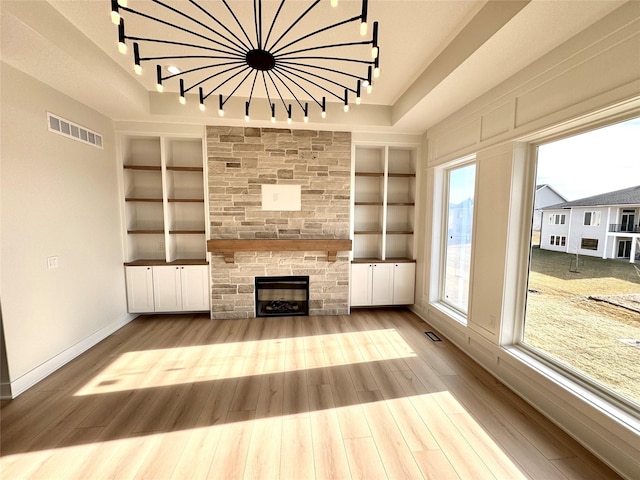 unfurnished living room featuring rail lighting, a stone fireplace, light hardwood / wood-style flooring, and built in shelves