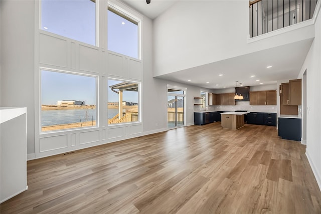 unfurnished living room with a towering ceiling, a water view, and wood-type flooring