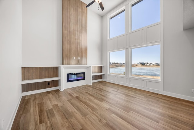 unfurnished living room featuring ceiling fan, a water view, light hardwood / wood-style flooring, and a towering ceiling