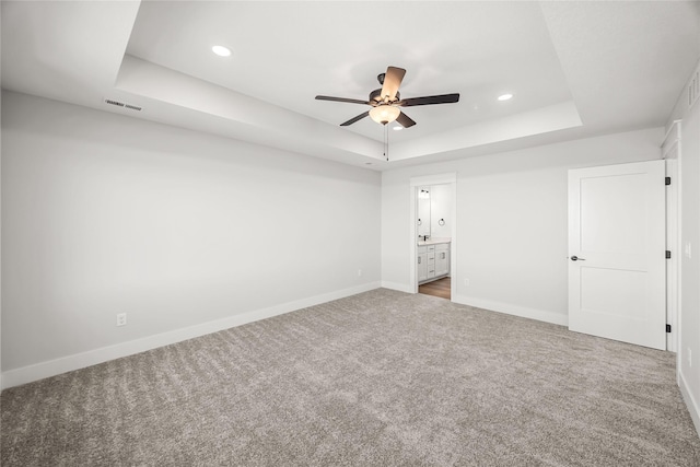 unfurnished bedroom featuring ceiling fan, ensuite bathroom, a raised ceiling, and carpet flooring