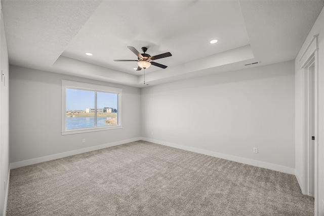 unfurnished room with ceiling fan, a raised ceiling, a water view, and carpet flooring